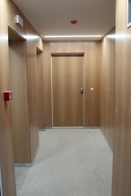 Corredor de edifício de habitação revestido a madeira, com porta de entrada a condizer