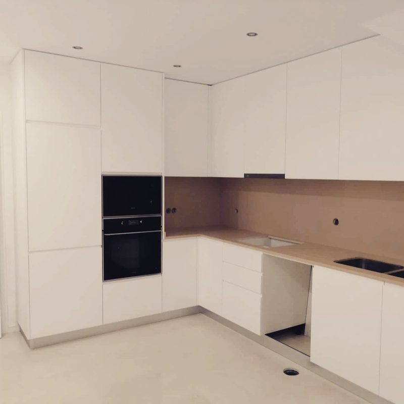 Cozinha branca em L até ao teto, com coluna de fornos e bancada clara