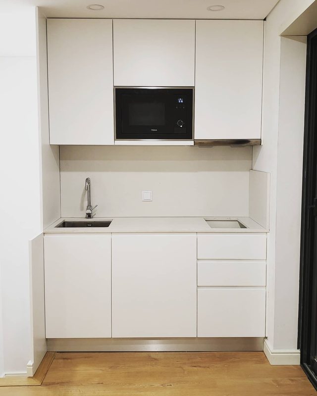 Cozinha compacta branca com micro-ondas encastrado, lava-loiça e gavetas