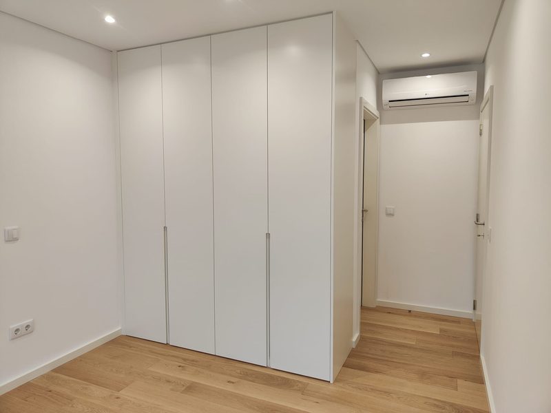 Roupeiro branco embutido de quatro portas com puxadores em linha, em quarto com pavimento de carvalho